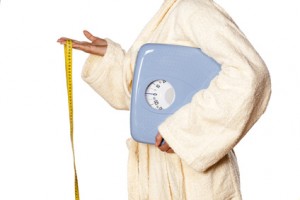 woman in bathrobe holding scales and a measuring tape